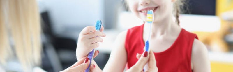 Dentist doctor holding two toothbrushes in front of little girl closeup. Daily oral hygiene as prevention of caries concept